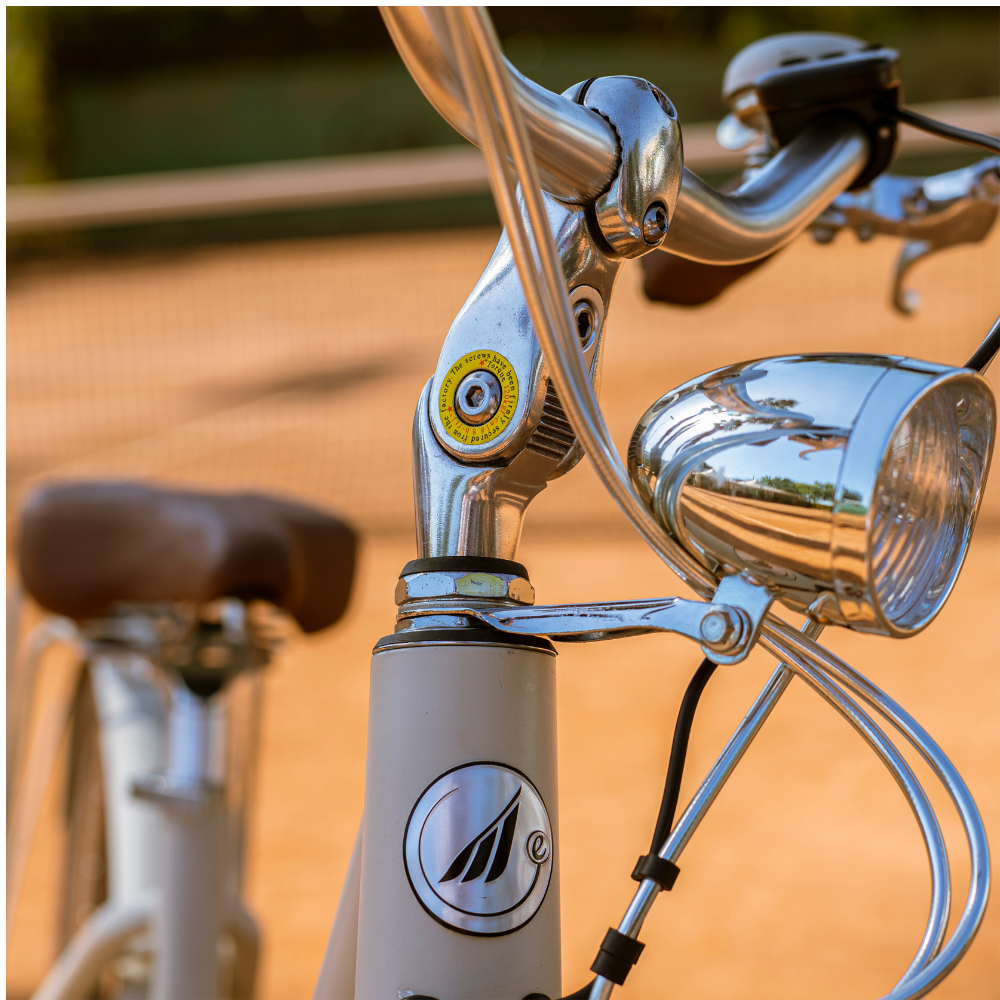 MBM La Rue Step thru electric bike, outside in a tennis court showing a close up of the handlebars and front light with MBM logo on the stem 