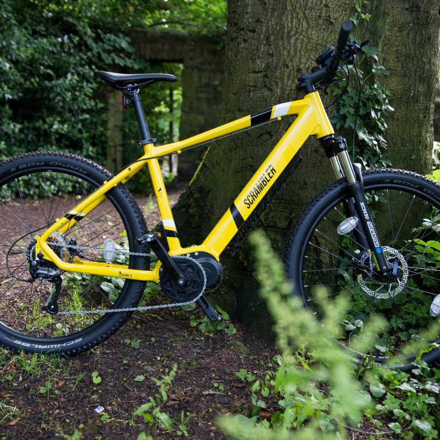 Mark2 Scrambler C Electric Mountain Bike, 90Nm Mid Drive, Top Speed 15.5MPH Yellow Leaning On A Tree