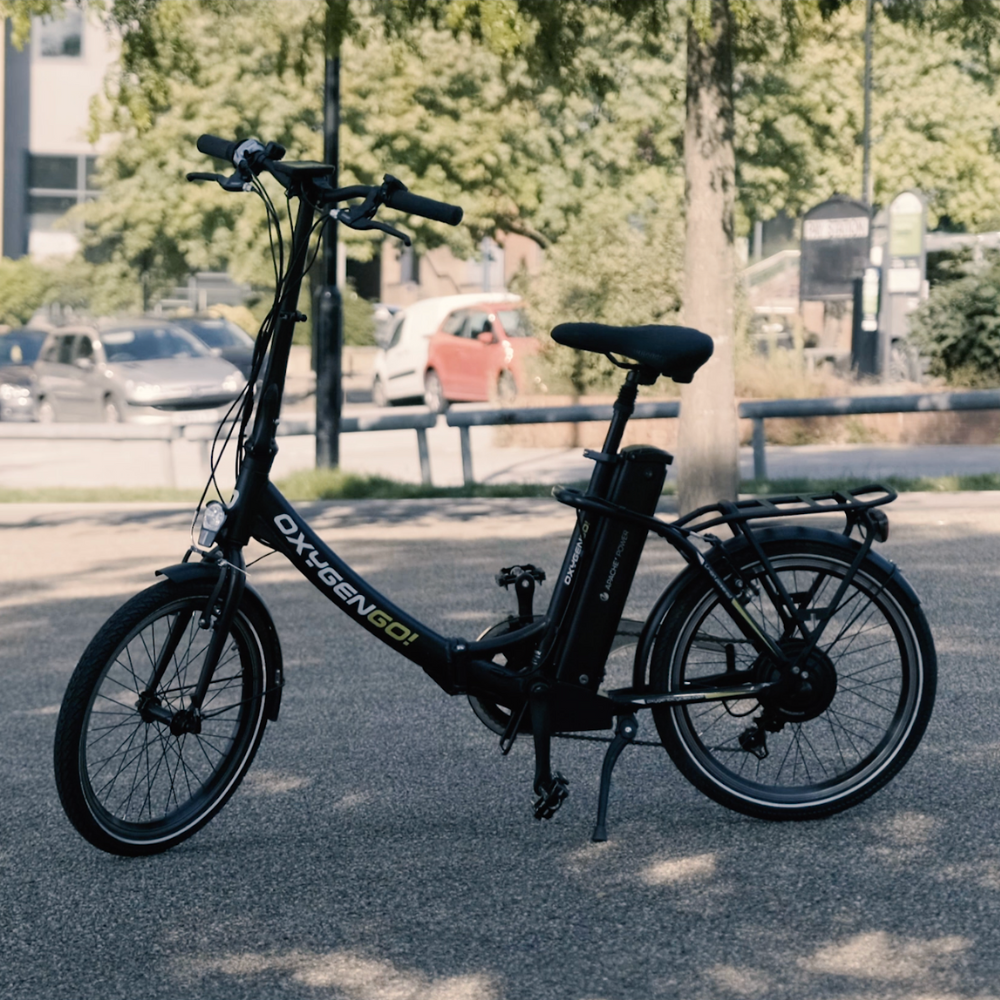 Oxygen Go Folding Step Thru Electric Bike, Urban, Black 15.5MPH Parked in a car park