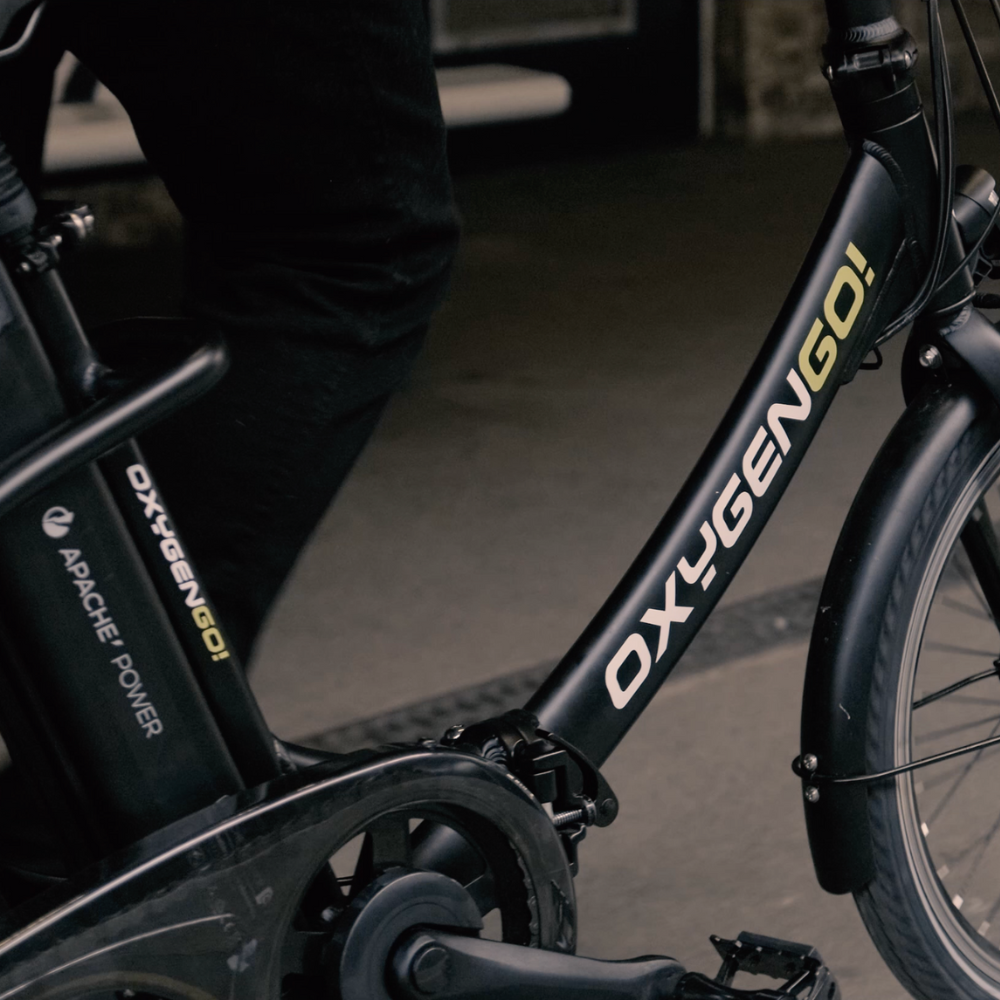 Oxygen Go Folding Step Thru Electric Bike, Urban, Black 15.5MPH Close up of the frame, logo and rear postitioned battery with the rider walking next to the bike