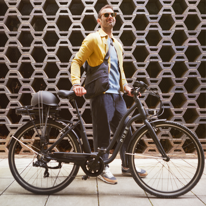 PURE Free City Step Thru Electric Bike, 15.5MPH with rider in front of architectural wall in diamond pattern 